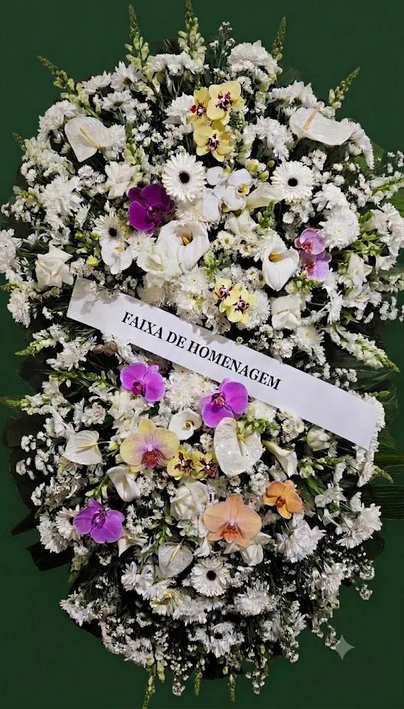 Coroa de flores brancas com orquídeas roxas, rosas, amarelas e pêssego, antúrios brancos e faixa de homenagem