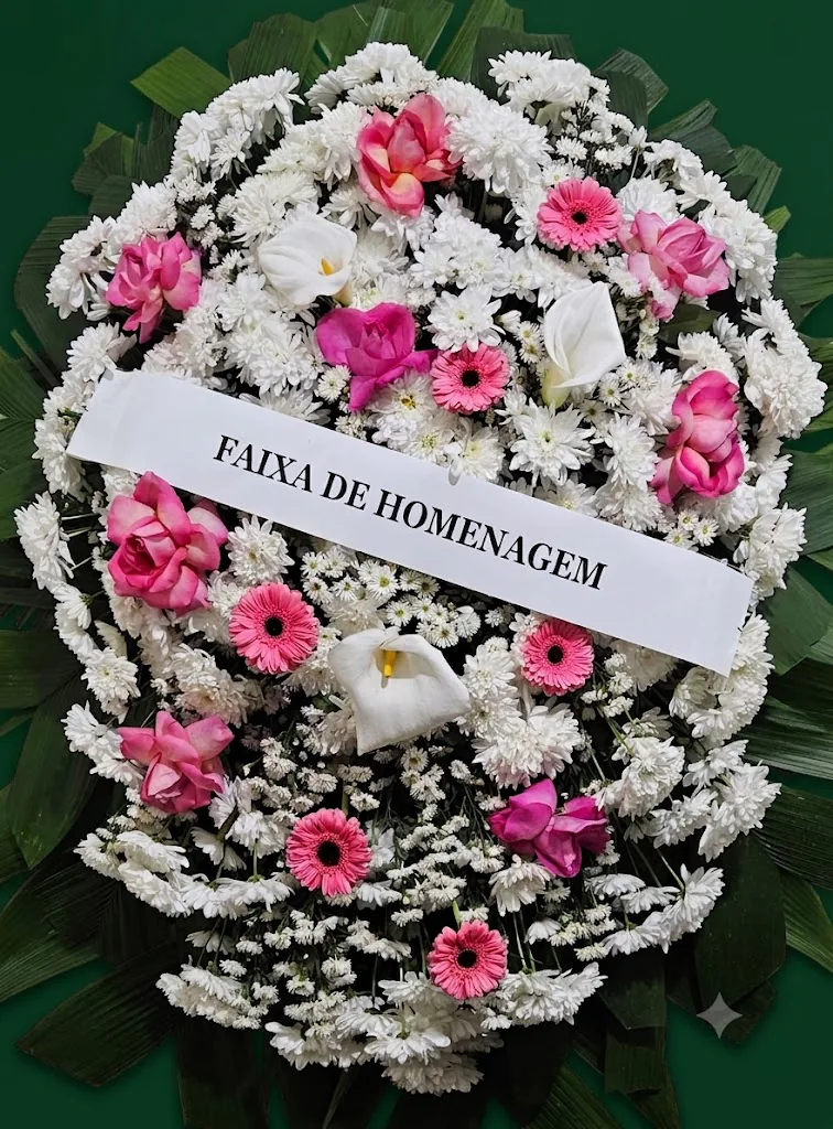 Coroa de flores brancas com rosas e gérberas cor-de-rosa, copos-de-leite e faixa de homenagem