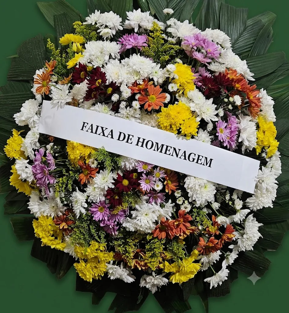Coroa de flores brancas com crisântemos amarelos, laranjas, roxos e vinho e faixa de homenagem
