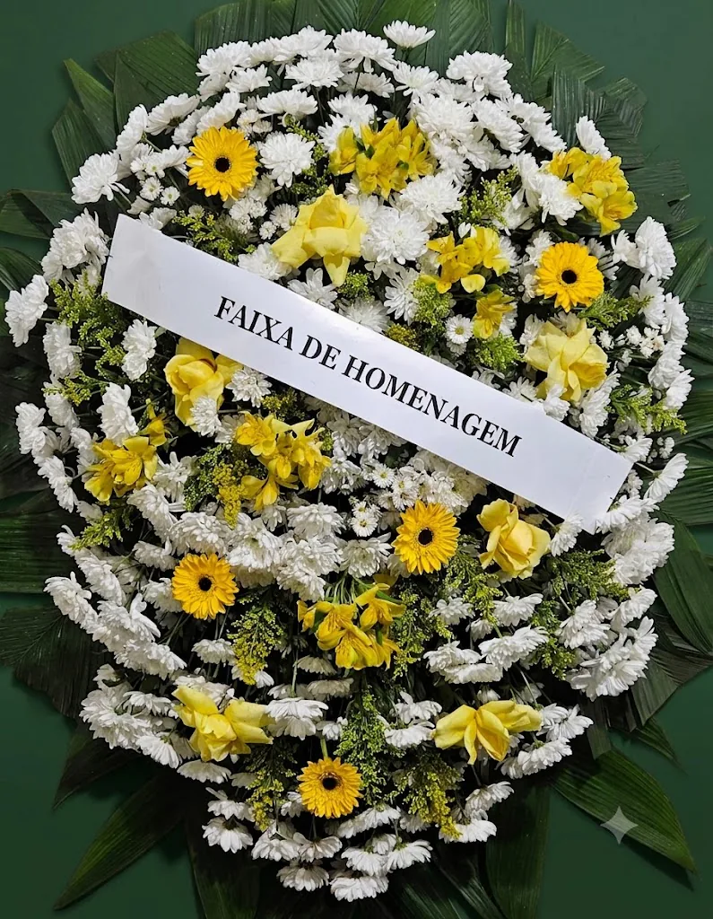 Coroa de flores brancas com rosas e gérberas amarelas e faixa de homenagem