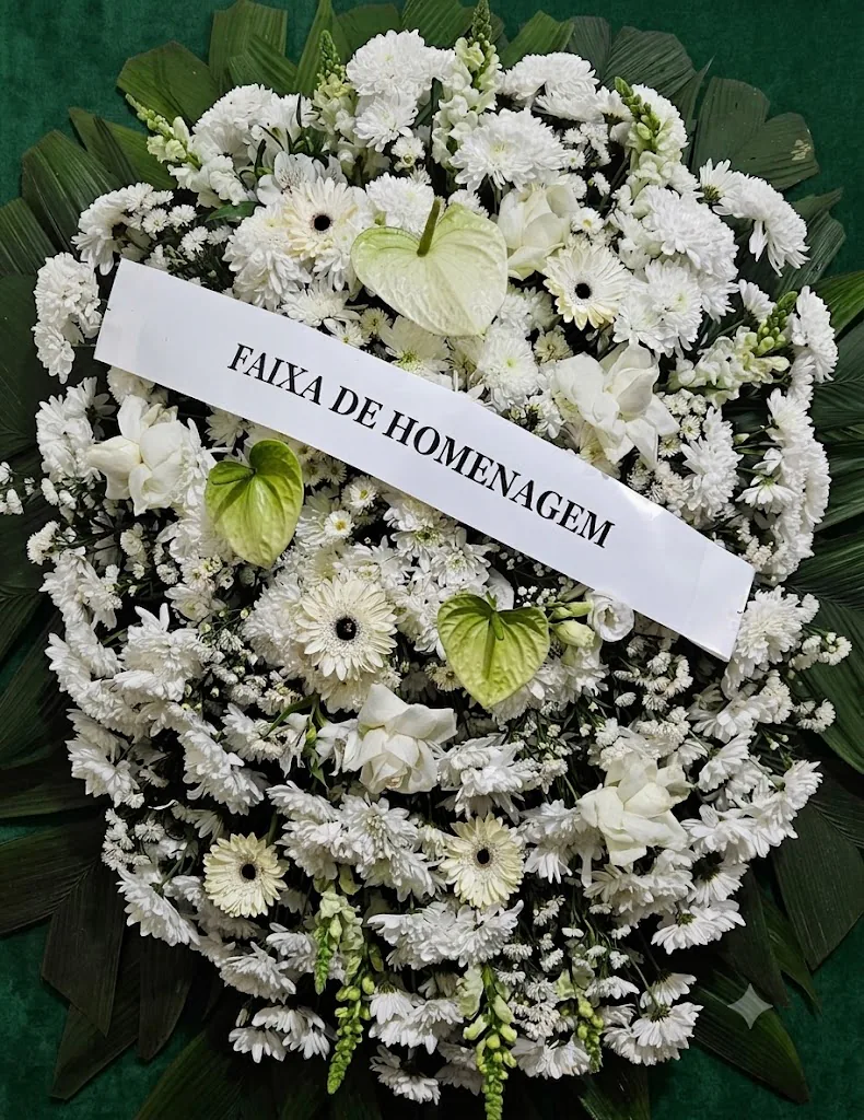 Coroa de flores brancas com antúrios esverdeados e faixa de homenagem