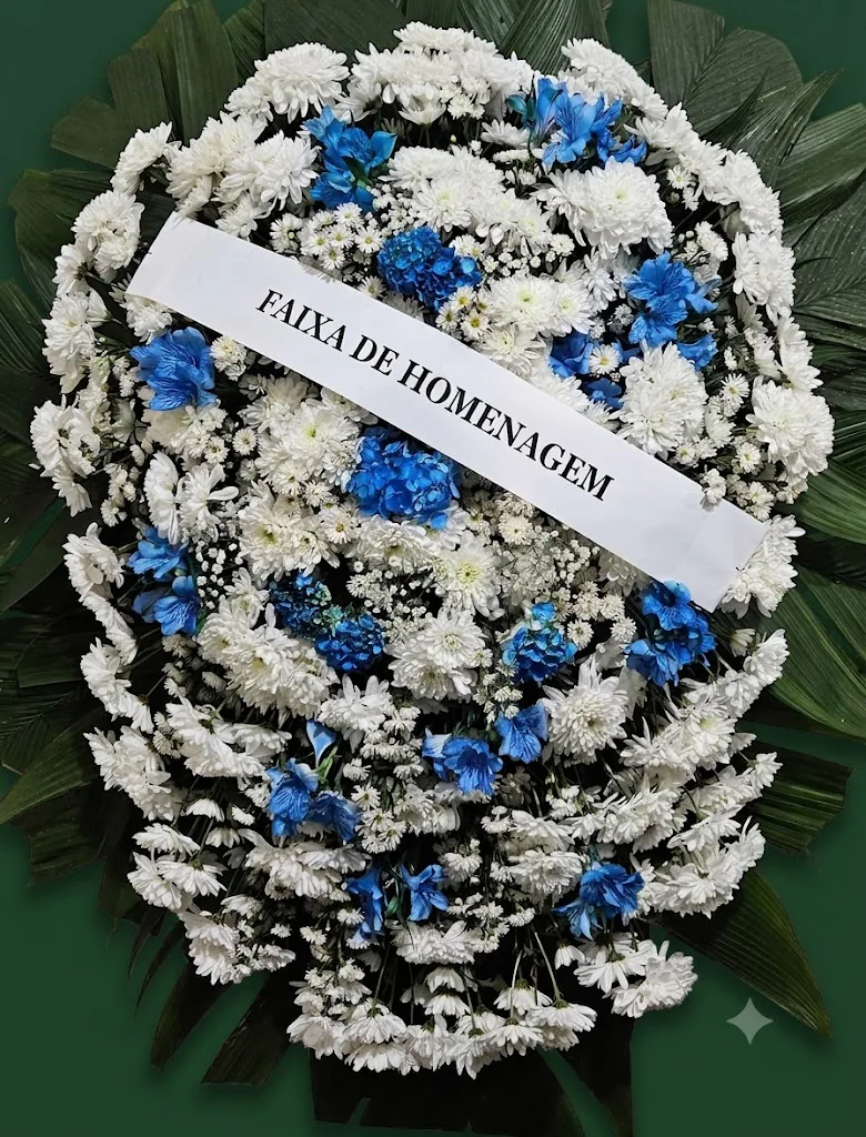 Coroa de flores brancas com flores azuis e faixa de homenagem