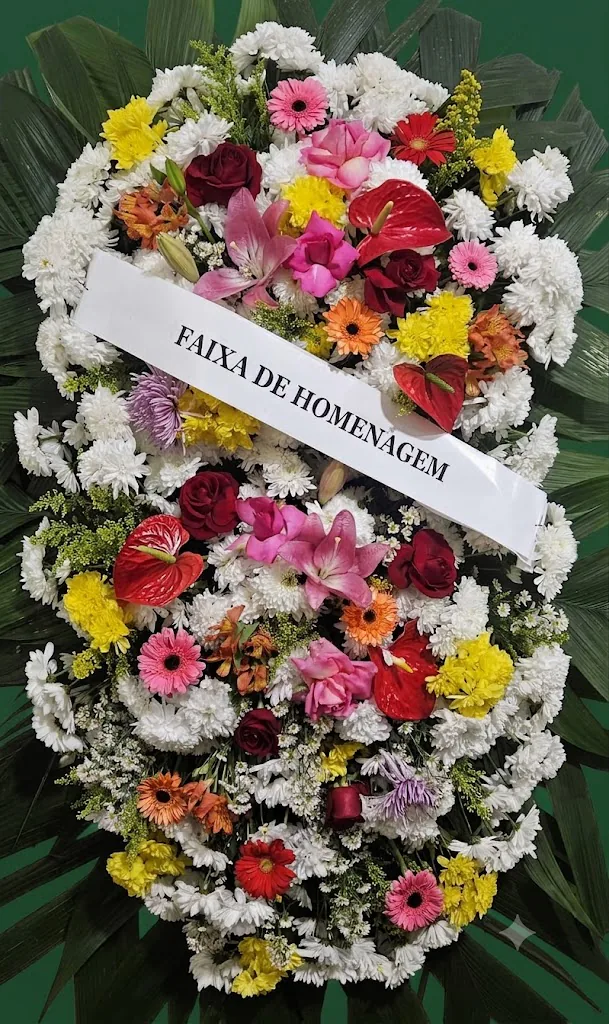 Coroa de flores coloridas com rosas vermelhas, lírios rosas, antúrios vermelhos e faixa de homenagem